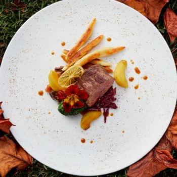 Küchenlinie Gourmet-Rindfleischgericht mit Wurzelgemüse und Garnitur auf weißem Teller zwischen Herbstblättern